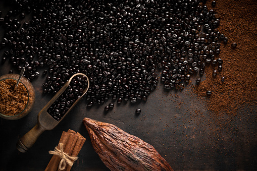 Black coffee beans dark black roast and scoop, cocoa pod, ground coffee, black sugar and cinnamon on wooden vintage background
