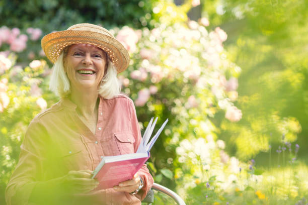 A senior woman reading a book in her garden in summer.