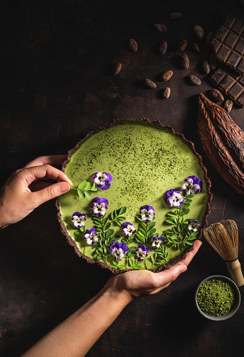Matcha tea and chocolate superfood tart with moringa leaves nuts and edible pansy flowers with cocoa pod and beans