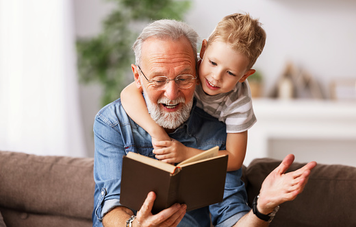 Smiling preteen girl with senior man in eyeglasses reading book together