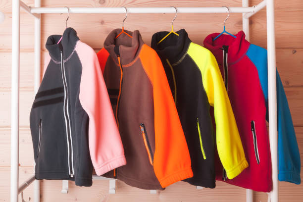 Colorful fleece jackets are hanging on hangers Colorful fleece jackets are hanging on hangers near wooden wall in a rack fleece photos stock pictures, royalty-free photos & images