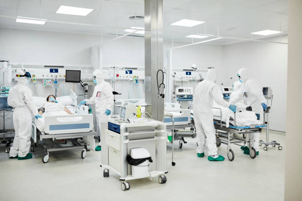 Healthcare Workers Treating Coronavirus Patients During Pandemic Doctors and nurses with patients in hospital. Healthcare workers are operating in ward. They are in protective workwear during COVID-19. intensive care unit photos stock pictures, royalty-free photos & images