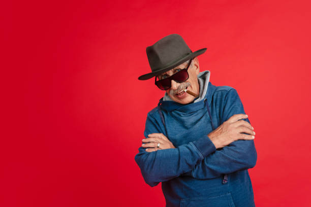 istock Senior man in stylish eyewear and hat isolated on red background. Tech and joyful elderly lifestyle concept 1277102738