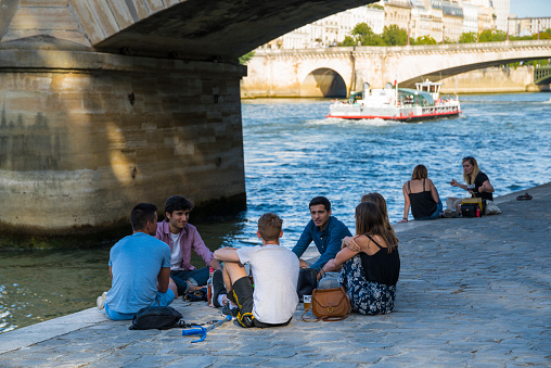 A group of young people enjoy a picnic on the banks of the Seine, next to one of the many bridges linking the two parts of the city of Paris. Parisians and tourists usually enjoy the banks of the river, which has become a real tourist attraction in the French capital.