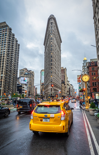 Woman hailing a yellow taxi on a busy street by Grand Central Terminal with American flags in the background