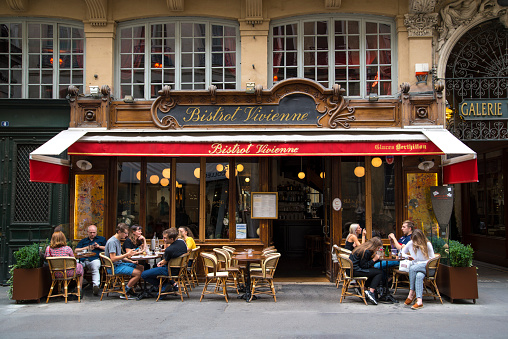 A group of tourists enjoy an aperitif at the tables of a Parisian bistro, next to the Galerie Vivienne, one of the most charming commercial passages in the city.