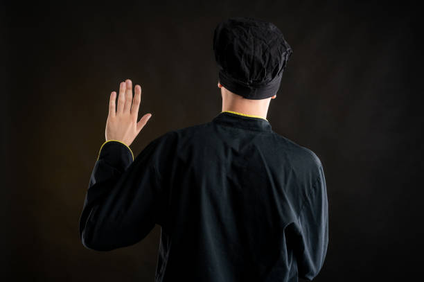 istock Young male dressed in a black chef suit showing oath from behind 1277110228