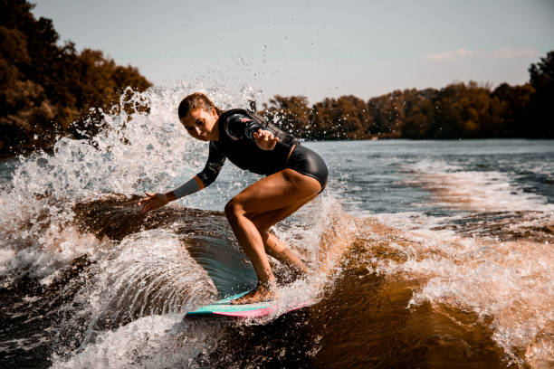 istock Beautiful woman stands with bent knees on surf style wakeboard and ride on wave 1277110394