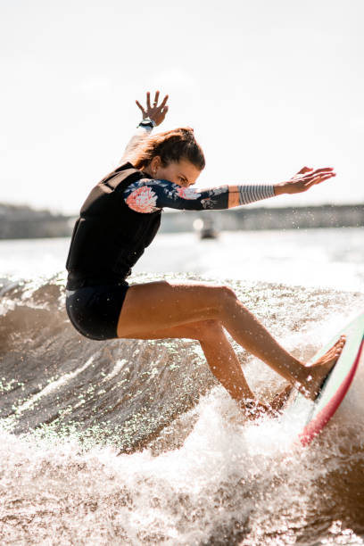 istock athletic woman stand on surf style wakeboard and ride up on splashed river wave. 1277111714