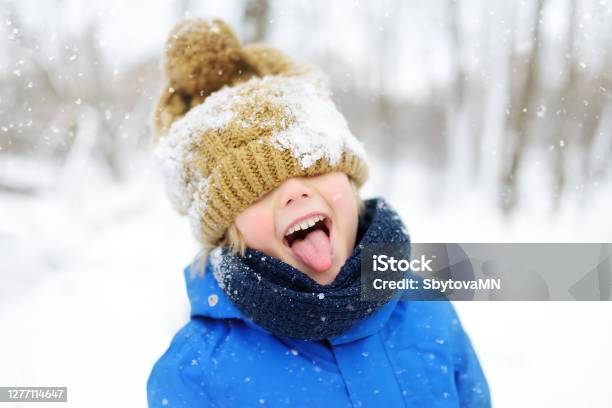 Funny Little Boy In Blue Winter Clothes Walks During A Snowfall Outdoors Winter Activities For Kids Stock Photo - Download Image Now