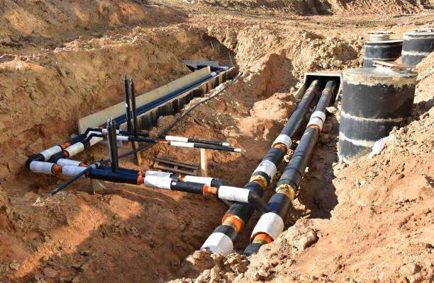 Laying heating pipes in trench at construction site. Installing concrete sewer wells and underground storm systems of sanitary water main Laying heating pipes in trench at construction site. Installing concrete sewer wells and underground storm systems of sanitary water main. Cold and hot water heating system of the apartments in house laying underground pipes stock pictures, royalty-free photos & images