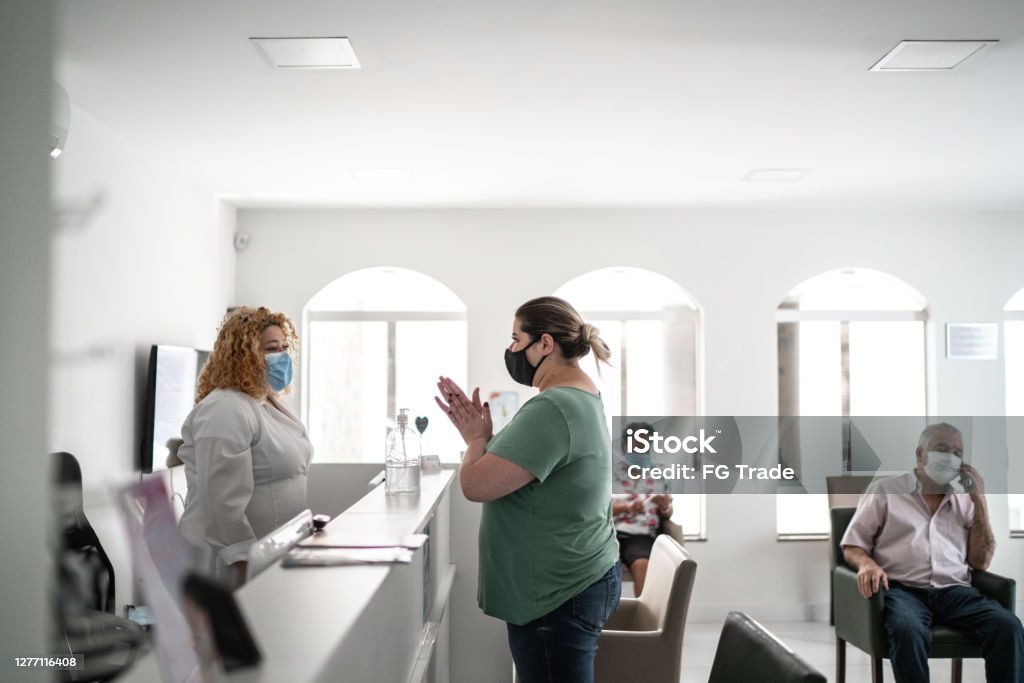 Patient arriving at medical clinic reception and using hand sanitizer Waiting Room Stock Photo