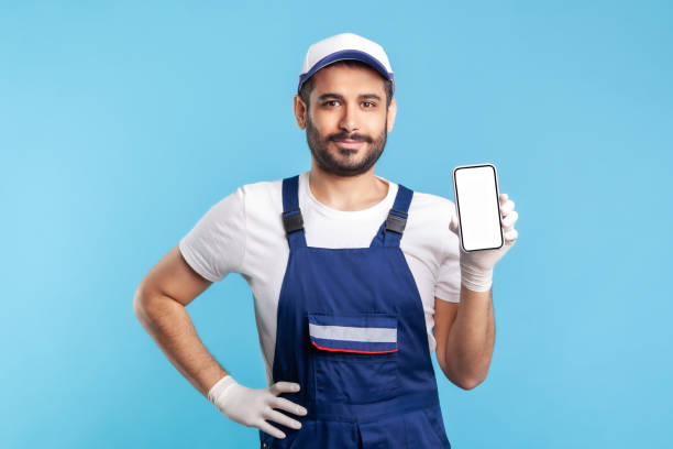 istock Worker in overalls and gloves holding mobile phone with blank display, device mock up for order app 1277118158