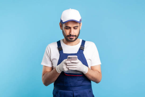 Handyman in overalls and gloves typing on mobile phone, using cellphone messenger to accept order