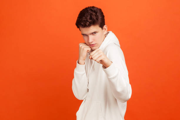 joven concentrado sosteniendo los puños apretados listos para boxear, manera masculina de resolver problemas. listo para defenderse de los delincuentes, el acoso - serious punching fighting displeased fotografías e imágenes de stock