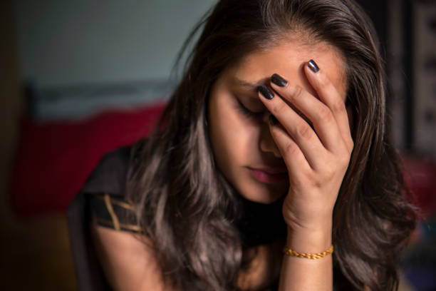 Portrait of young girl holding her head and feeling headache. indoor image of sad, depressed young girl feeling headache and thinking by holding her head and looking down at home. facepalm stock pictures, royalty-free photos & images