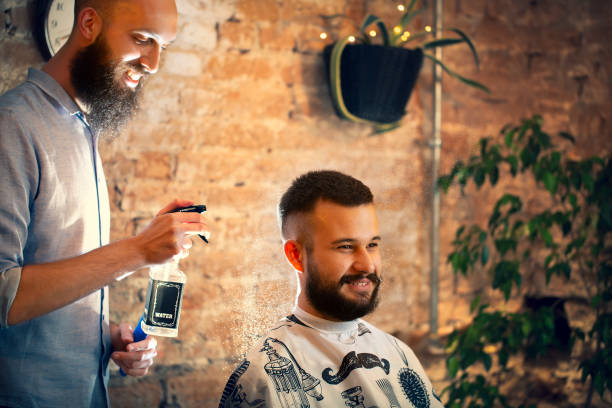 Hairdresser using hair spray on client hair at barber shop. Good looking man visiting barber shop. stock photo