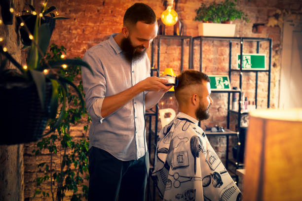 Good looking man visiting barber shop. The barber cuts his hair and trims his beard. stock photo