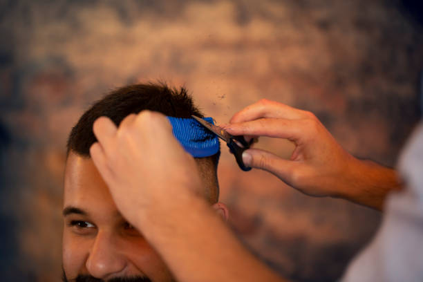 Good looking man visiting barber shop. The barber cuts his hair and trims his beard. stock photo