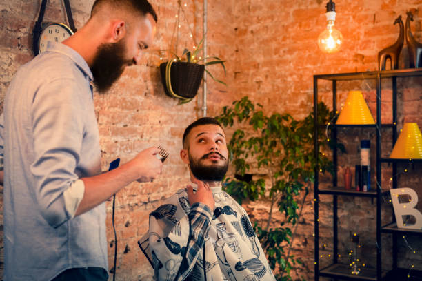 Good looking man visiting barber shop. The barber cuts his hair and trims his beard. stock photo