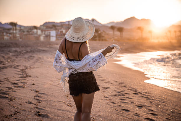 istock A woman in a hat walks at sunset on the beach rear view 1277126514