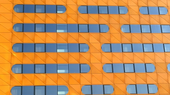 Orange Facade of building with pattern of oval shaped mirror windows. Modern architecture background. Beauty of skyscraper geometry. Design and construction industry concept. Urban real estate. Office