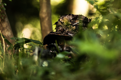 A hunter in full camouflage is hunting in the jungle with his M4.