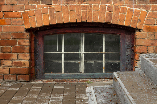 A window in the basement of an old brick building and a concrete staircase.