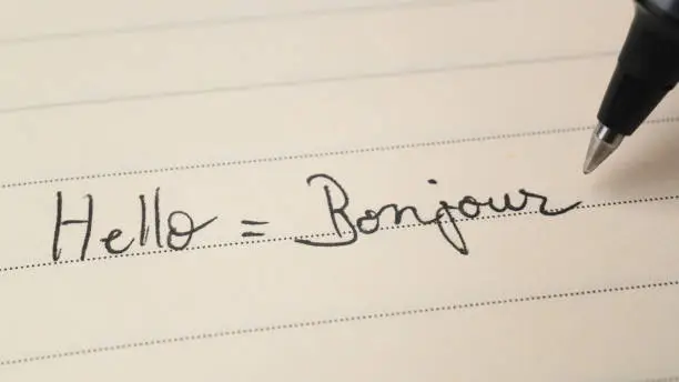 Beginner French language learner writing Hello word Bonjour for homework on a notebook macro shot