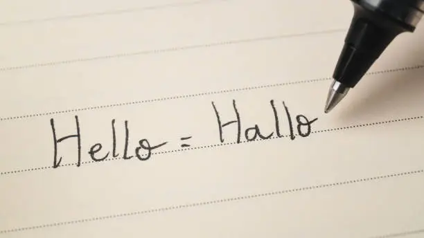 Photo of Beginner German or Dutch language learner writing Hello word Hallo for homework on a notebook macro shot