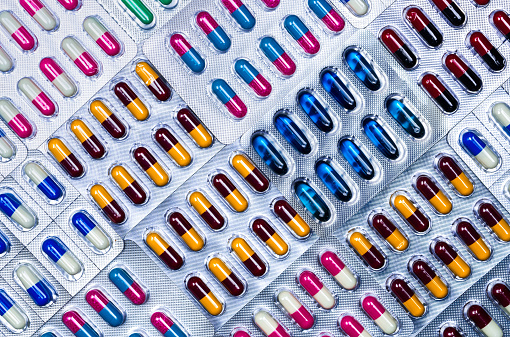 Top view of capsule pills in blister pack. Pharmaceutical industry. Pharmaceutical manufacturing industry concept. Capsule pills production. Full frame shot of blue, pink, yellow, red, black capsules.