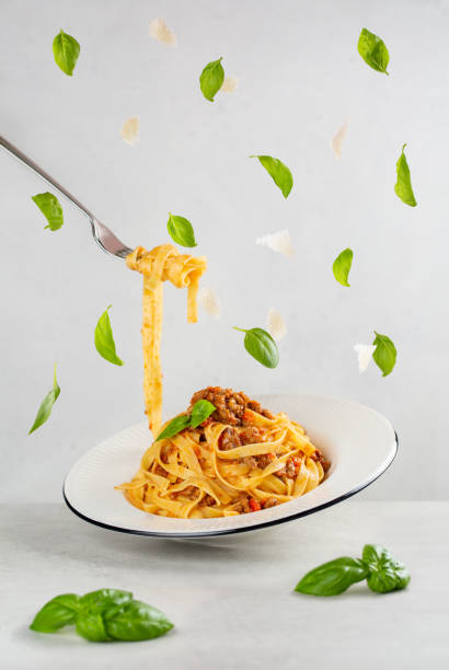 manger des pâtes italiennes avec de la viande bolognaise et de la sauce tomate. feuilles de basilic flottantes et paix du parmesan. photo dynamique avec lévitation. fond gris clair. - dishware pasta tagliatelle beef photos et images de collection