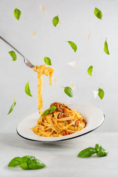 Eating Italian pasta with bolognese meat and tomato sauce. Floating basil leaves and peace of parmesan cheese. Dynamic photo with levitation. Light grey background. Eating Italian pasta with bolognese meat and tomato sauce. Floating basil leaves and peace of parmesan cheese. Dynamic photo with levitation. Light grey background. levitation photos stock pictures, royalty-free photos & images