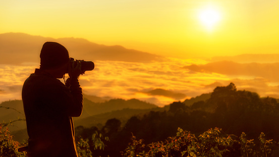 Silhouette professional man photographer holding camera for take a photo the mountain  field during mist sunrise nature.  Tourism travel in attraction place tourist travel leisure and destination in Thailand