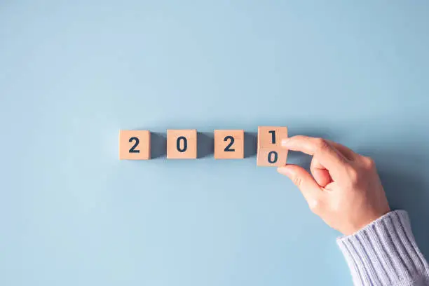 Photo of Hand flipping wooden blocks for change year 2020 to 2021 on blue paper background.