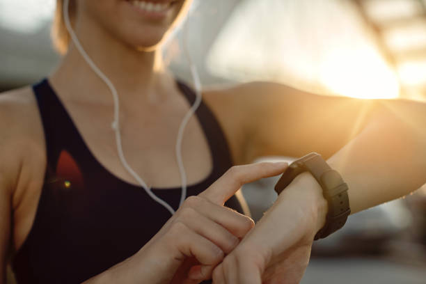 Close-up of athletic woman using fitness tracker at sunset. Close-up of female athlete using fitness tracker while practicing outdoors at sunset. fitness tracker photos stock pictures, royalty-free photos & images