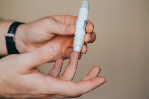 istock Close up of a man's hand using a lancet on his finger to check blood sugar using a glucose meter, using as medicine, diabetes, glycemia, healthcare and people concept. 1277141579
