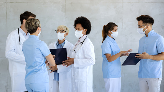 Group of doctors and nurses wearing protective face masks while communicating in a lobby at medical clinic.