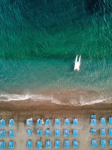 Aerial view of a beach with umbrellas and a rowboat. Blue sunbeds and white rowboat in a turquoise sea.