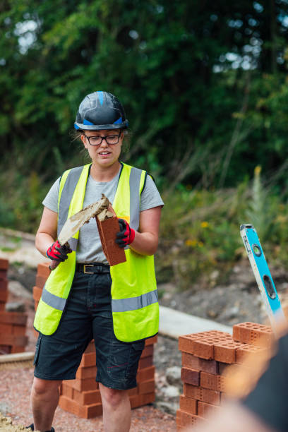 Getting Stage One Started A shot of a Caucasian female construction worker putting cement on a brick with a trowel. helmet hardhat protective glove safety stock pictures, royalty-free photos & images