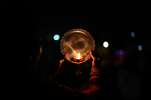 Young Indian woman celebrating Karva Chauth at night. Karva Chauth is a one-day festival celebrated by Hindu women four days after purnima (a full moon) in the month of Kartika. On Karva Chauth women, especially in Northern India, who are married fast from sunrise to moonrise for the safety and longevity of their husbands.