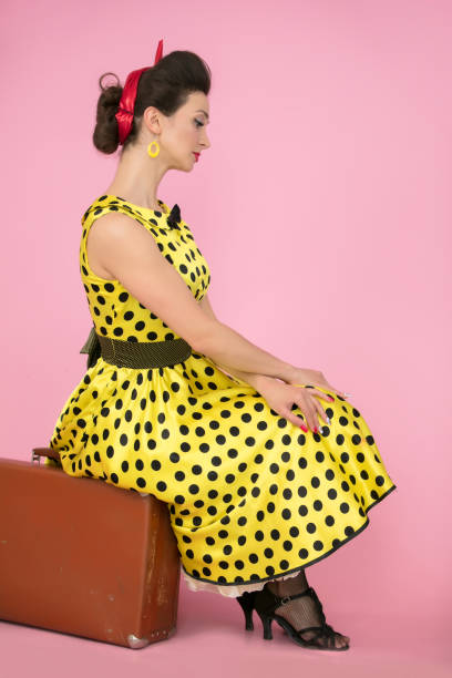 belle fille de pin-up sur un fond rose. femme rétro dans la robe jaune de point de polka. fille avec une vieille valise. concept de voyage. - polka dot suitcase retro revival women photos et images de collection