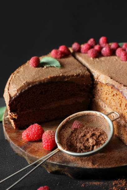 istock Chocolate cake with raspberries. Cake on a dark background. Sieve with cocoa powder. 1277153635