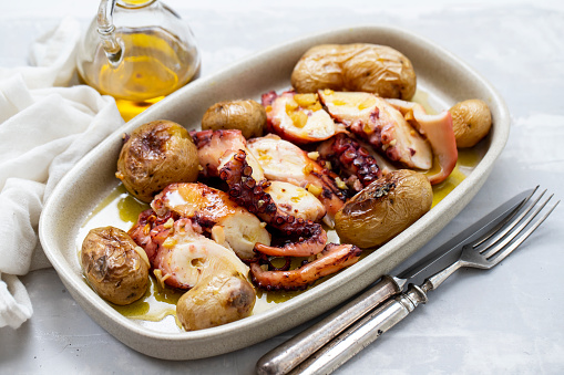 grilled octopus with potato, olive oil on white dish on ceramic background