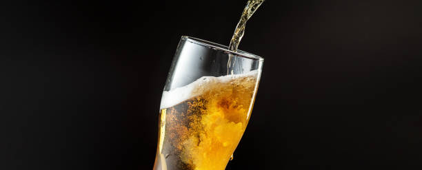 Pouring of cold and refreshing beer in glass with foam, horizontal flyer Pouring of cold and refreshing beer in glass with foam, horizontal flyer with copyspace for ad. Beer Fest, drinks, alcohol, party concept. Brewed and crafted quality product on dark background. pouring stock pictures, royalty-free photos & images