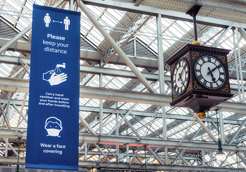 A large public health banner advising people to keep a safe distance, keep their hands clean, and wear a face covering, posted in Glasgow Central Station for passenger safety during the Covid-19 pandemic.