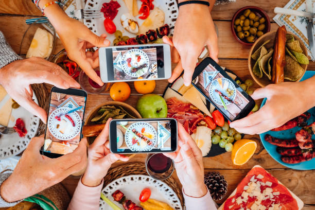 vista dall'alto del gruppo di persone durante la notte di natale scattando foto di cibo e piatti con lo smartphone tutti insieme - concetto di tradizione di festa con la famiglia e gli amici e tecnologia - food photography foto e immagini stock