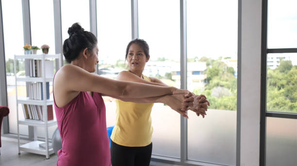 istock Young asian woman is relaxing in practicing stretching yoga poses while standing with her personal trainer. Restorative asana for spine stretching. Females performing yoga on exercise mat at gym. 1277174093