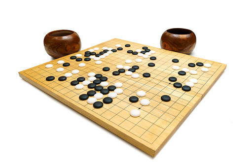 black and white stones on a ‘GO’ board made from wood on white background - traditional chinese strategy board game (called Baduk in Korea, Weiqi in China, iGo in Japan)