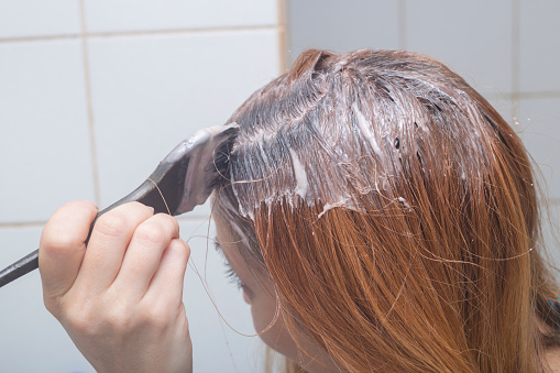 Adult female self dying her hair in bathroom at home.